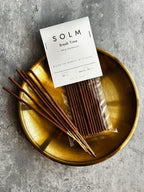真鍮色の丸いトレーに置かれたSOLM「Break Time」のパッケージとお香スティック